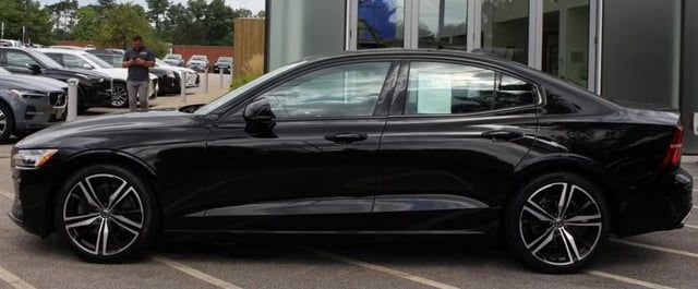 Svart Volvo S60, sedd från sidan, parkerad utanför en bilhall.